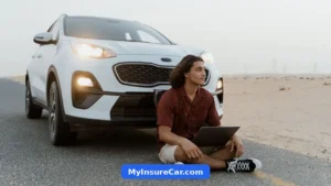 A young man sitting on a road in front of a white SUV, using a laptop