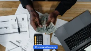 Hands counting dollar bills beside a calculator, laptop and documents
